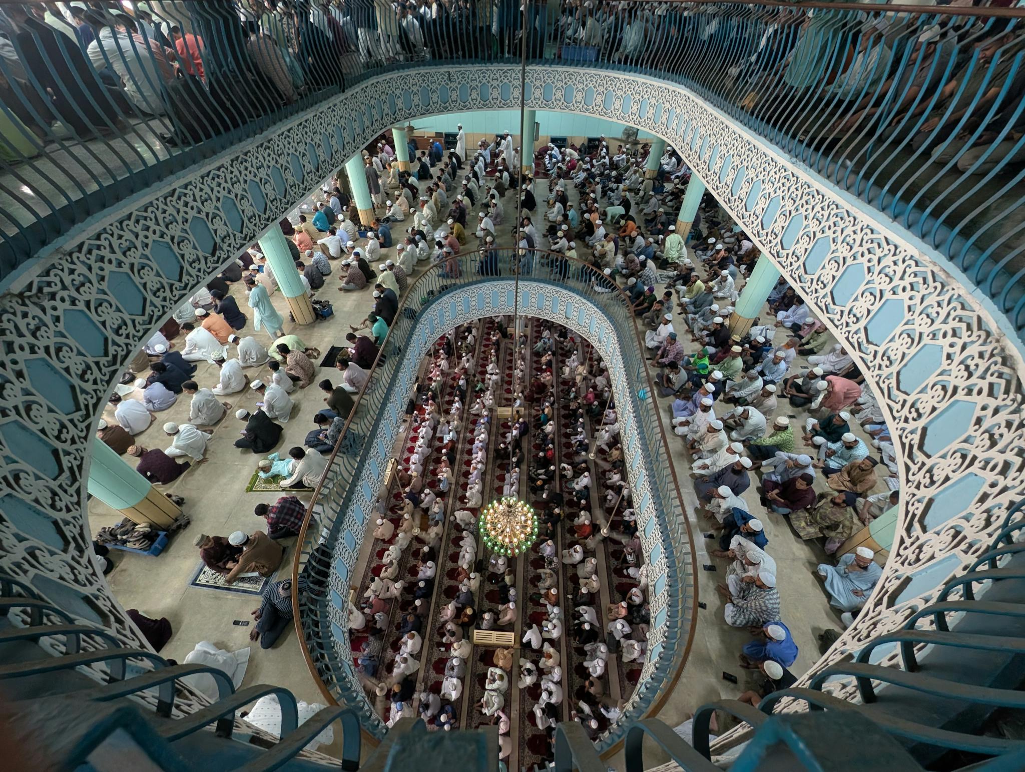 Aerial shot of people praying inside a beautifully decorated mosque, showcasing Islamic architecture.