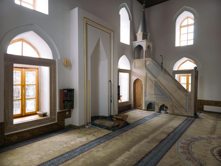 Sunlit interior of a serene mosque featuring wooden windows and a mihrab with intricate design.