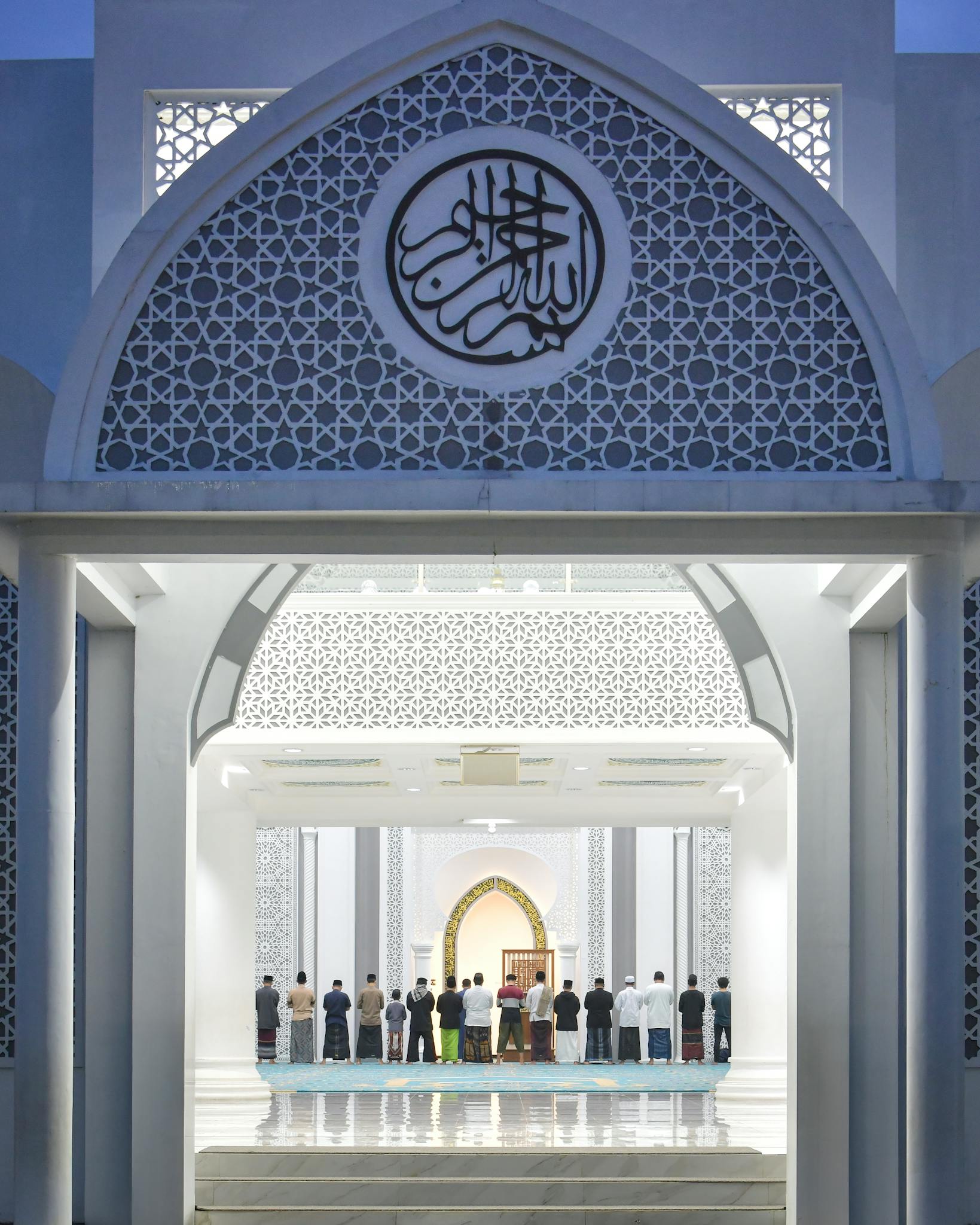 Worshippers gather for prayer in a beautifully lit Indonesian mosque at dusk.